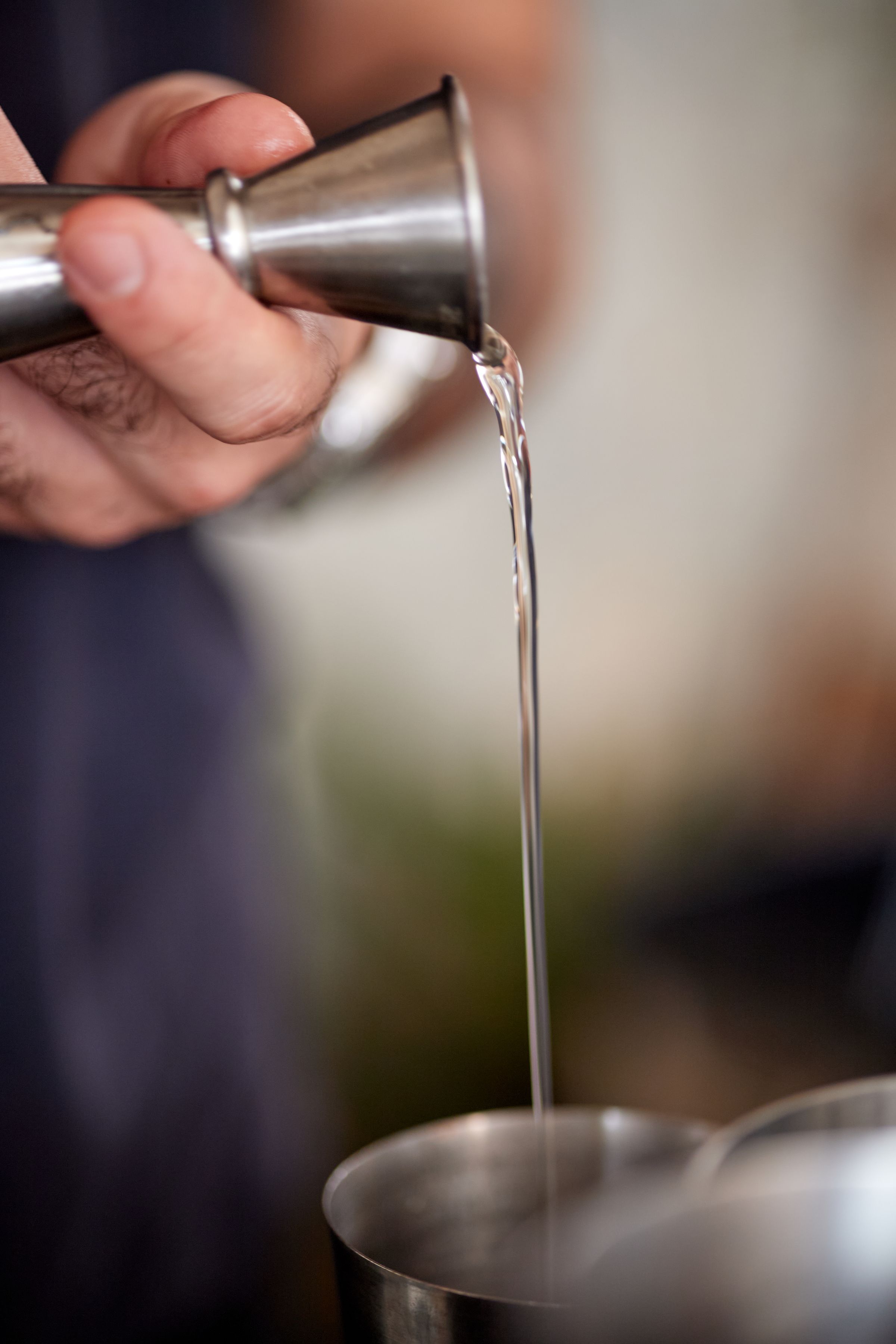 Bartender pouring from a jigger into a shaker tin