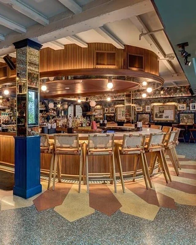 Wood-paneled round bar with rattan stools under a copper canopy at Red Rooster in Miami