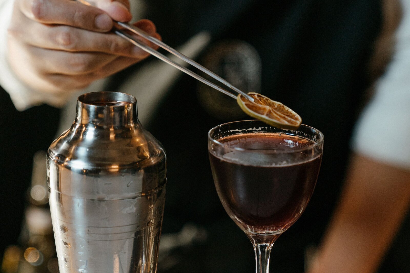 Bartender placing a garnish on a coupe with tweezers